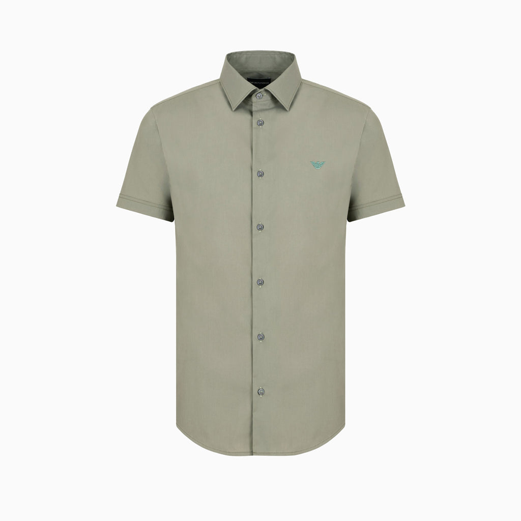 A short-sleeve button-down shirt in a muted sage green color, featuring a small embroidered bird logo on the left chest, displayed on a clean white background. Emporio Armani Short Sleeved Shirt. Sakks Menswear Southampton.