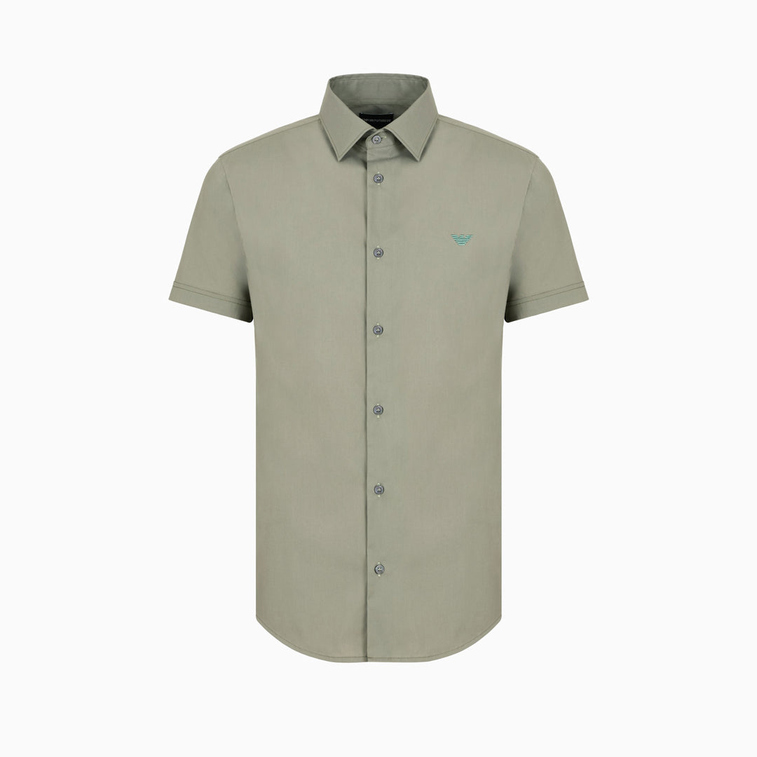 A short-sleeve button-down shirt in a muted sage green color, featuring a small embroidered bird logo on the left chest, displayed on a clean white background. Emporio Armani Short Sleeved Shirt. Sakks Menswear Southampton.