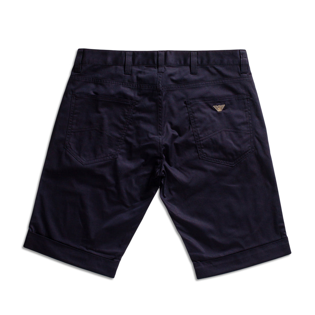 Dark navy blue chinos shorts shown from the back, featuring a belt loop, two rear patch pockets, and a small gold embroidered eagle logo on the right pocket, set against a plain white background. Emporio Armani Shorts. Sakks Menswear Southampton.