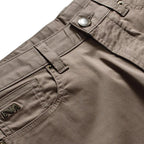 Close-up of the waistband and front pocket of taupe brown pants, showing a silver metal button, belt loops, and a small embroidered logo patch on the pocket. Emporio Armani Shorts. Sakks Menswear Southampton.