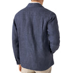 A man viewed from the back wearing a textured navy blue long-sleeve linen shirt jacket, paired with beige trousers, against a plain white background. Eton Shirt Jacket available at Sakks Menswear in Southampton.