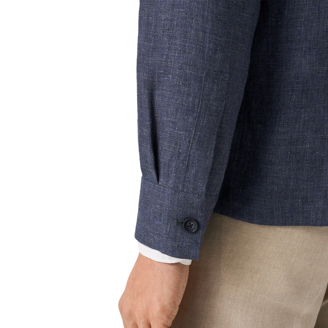 Close-up of a navy blue textured blazer sleeve with a button cuff, worn with beige trousers and a white dress shirt cuff visible, on a white background. Eton Shirt Jacket available at Sakks Menswear in Southampton.