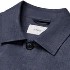 Close-up of a textured navy blue collared shirt with a white neck label reading ETON and a dark button, shown against a white background. Eton Shirt Jacket available at Sakks Menswear in Southampton.