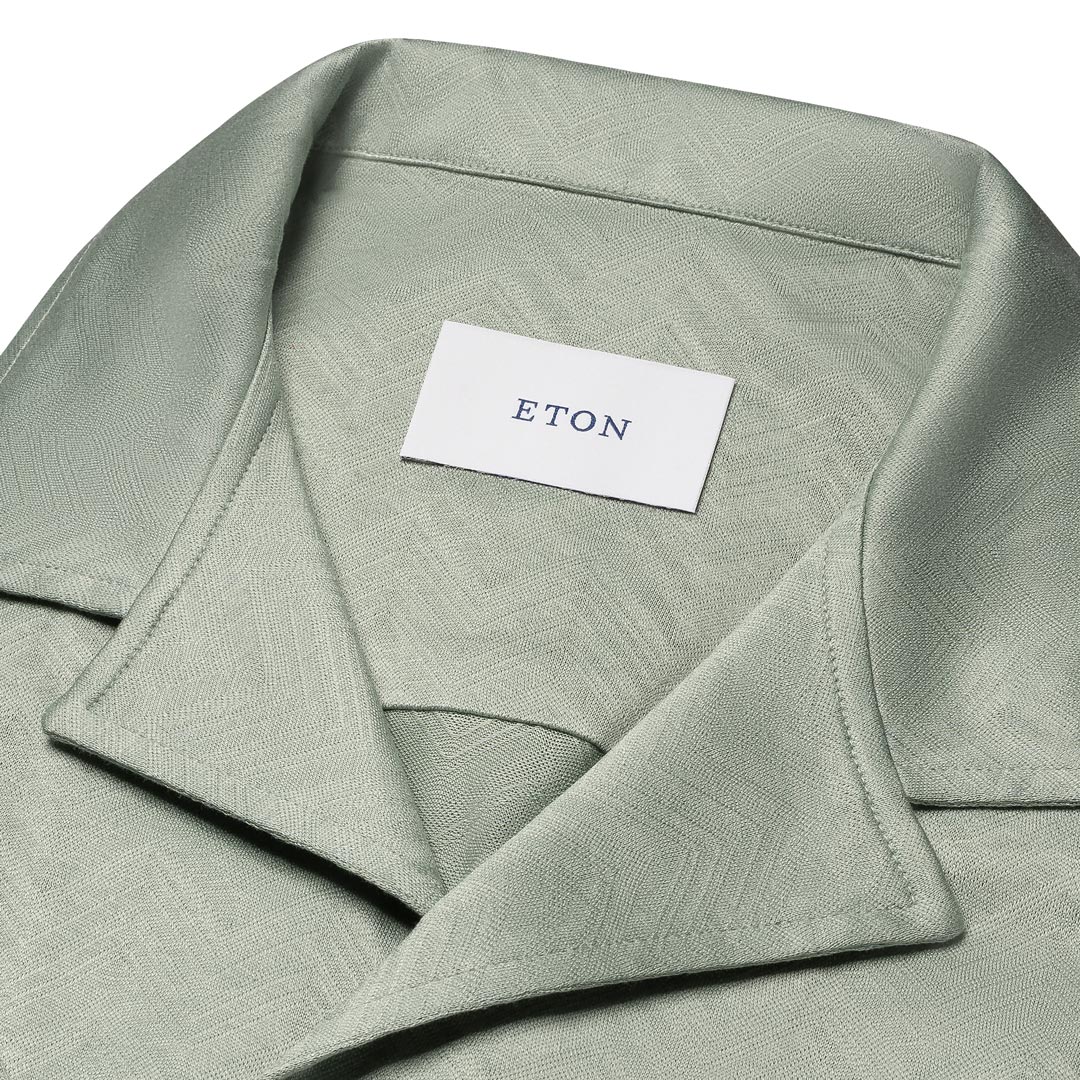Close-up of a light sage green collared shirt with a subtle geometric pattern, featuring a white neck label with the brand name 'ETON'. Eton Short Sleeve Shirt available at Sakks Menswear in Southampton.