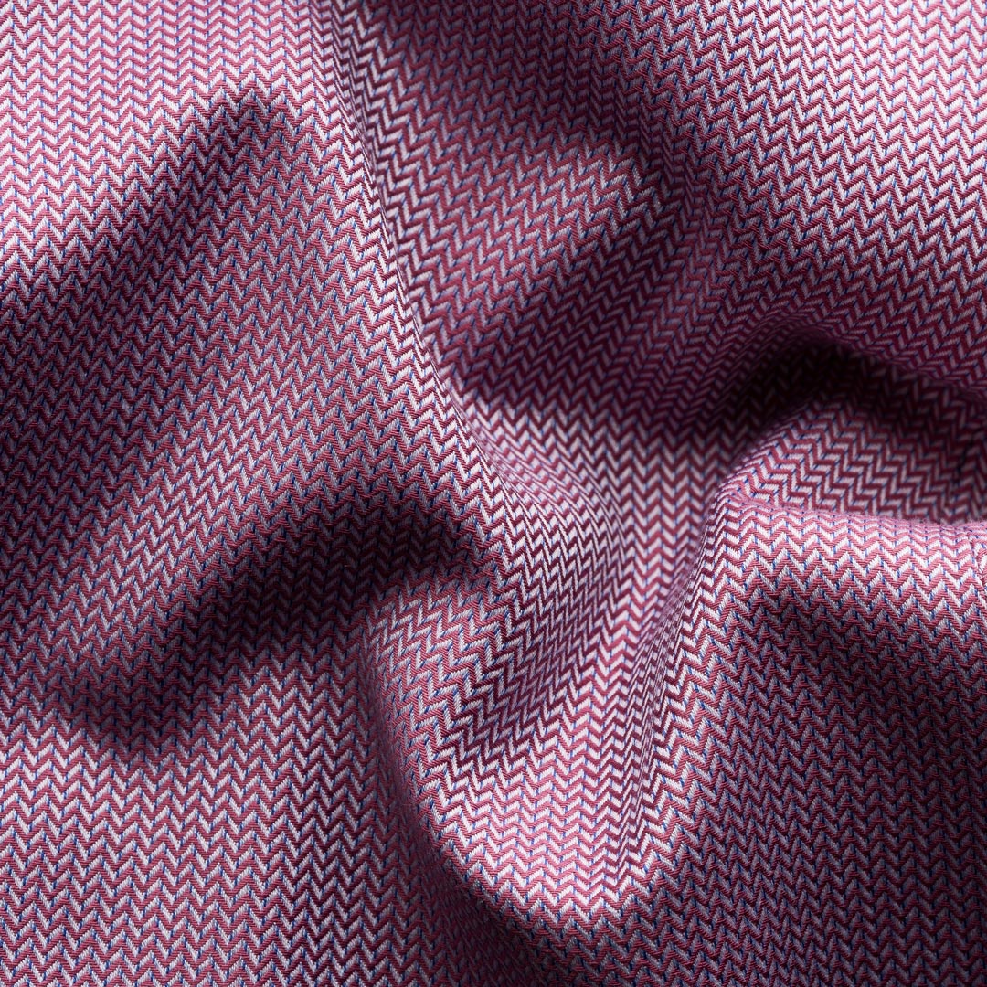 A close-up of draped fabric with a fine herringbone pattern in dusty purple and pink tones, showing soft folds and shadows. Eton Shirt available at Sakks Menswear in Southampton.