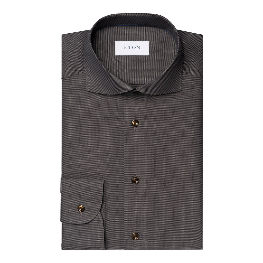 A dark grey textured dress shirt folded neatly, featuring a pointed collar, a chest pocket with a buttoned cuff, and dark brown buttons. The brand label 'ETON' is visible inside the collar. Eton Shirt available at Sakks Menswear in Southampton.