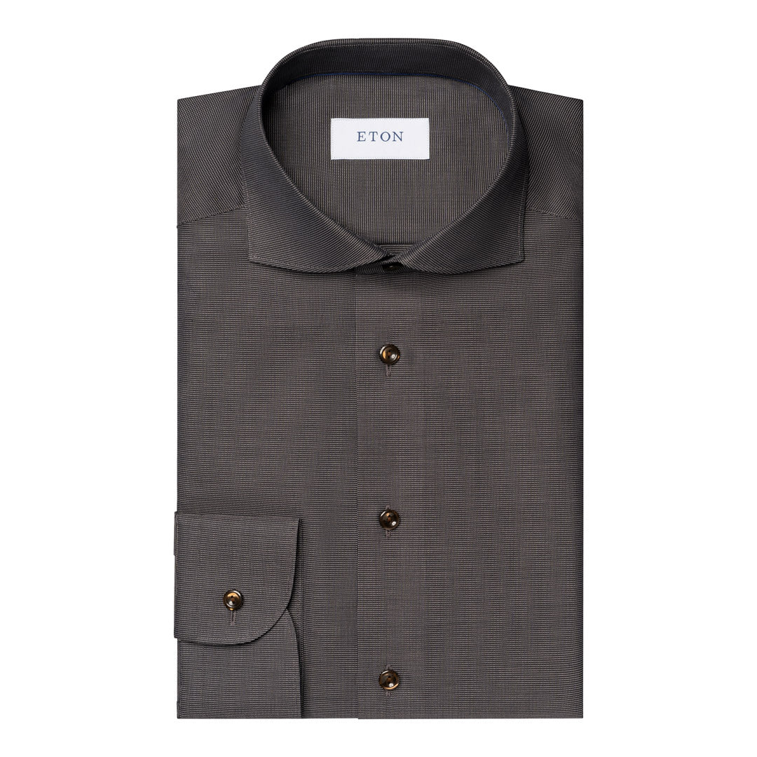 A dark grey textured dress shirt folded neatly, featuring a pointed collar, a chest pocket with a buttoned cuff, and dark brown buttons. The brand label 'ETON' is visible inside the collar. Eton Shirt available at Sakks Menswear in Southampton.