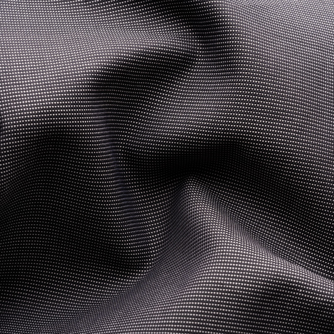 A close-up of a black fabric with a fine, repeating white dotted pattern, shown with soft folds and shadows. Eton Shirt available at Sakks Menswear in Southampton.