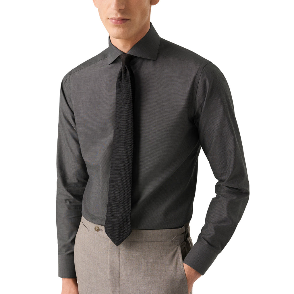 A man wearing a dark charcoal gray long-sleeve dress shirt with a matching dark tie and light gray trousers, shown from the chin down against a plain white background. Eton Shirt available at Sakks Menswear in Southampton.