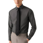 A man wearing a dark charcoal gray long-sleeve dress shirt with a matching dark tie and light gray trousers, shown from the chin down against a plain white background. Eton Shirt available at Sakks Menswear in Southampton.