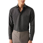 A man wearing a dark charcoal grey long-sleeve button-down dress shirt tucked into gray trousers, shown from the chin down against a plain white background. Eton Shirt available at Sakks Menswear in Southampton.