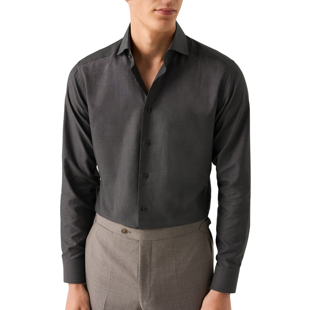 A man wearing a dark charcoal grey long-sleeve button-down dress shirt tucked into gray trousers, shown from the chin down against a plain white background. Eton Shirt available at Sakks Menswear in Southampton.