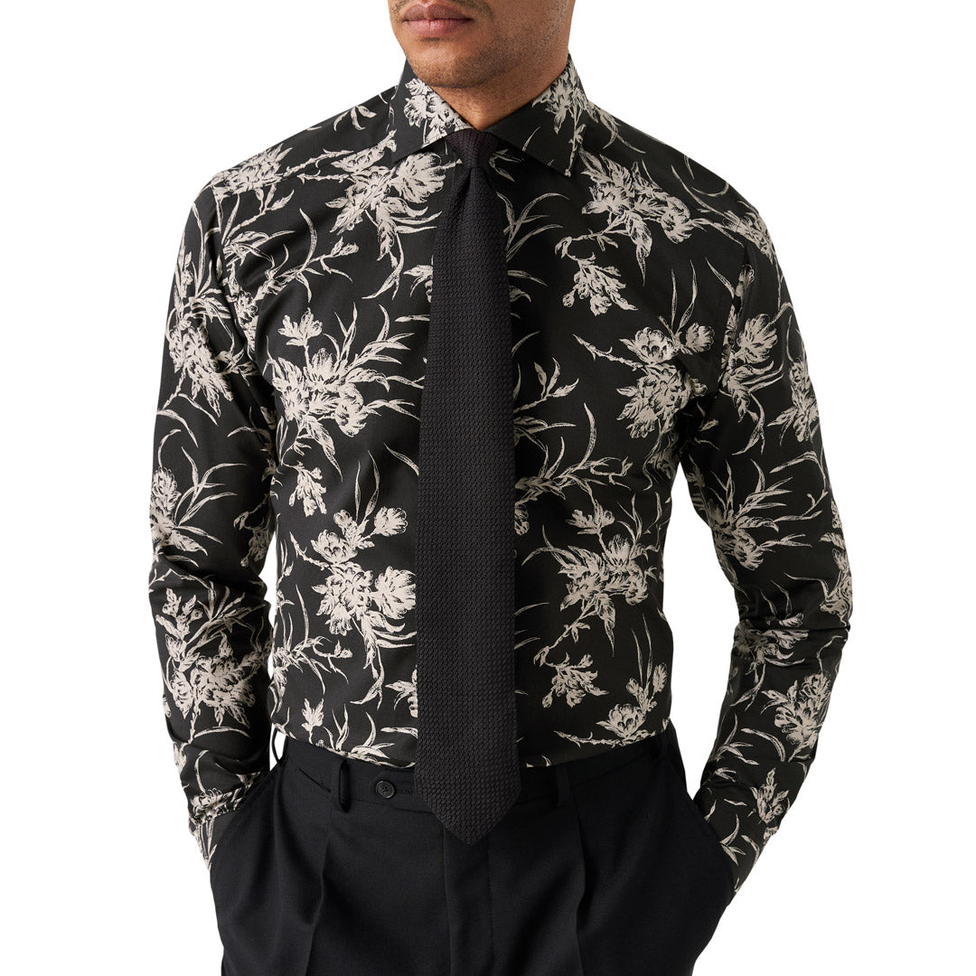 A man wearing a black long-sleeve dress shirt with a beige floral pattern, paired with a black tie and black trousers, shown from the chin down against a white background. Eton Shirt available at Sakks Menswear in Southampton.