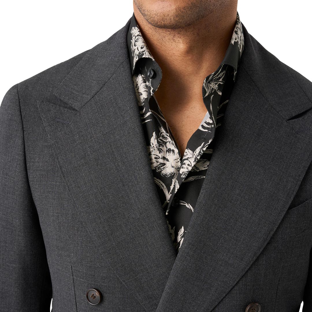 A close-up of a man wearing a dark gray double-breasted suit jacket over a black and white patterned silk shirt, against a plain white background. Eton Shirt available at Sakks Menswear in Southampton.
