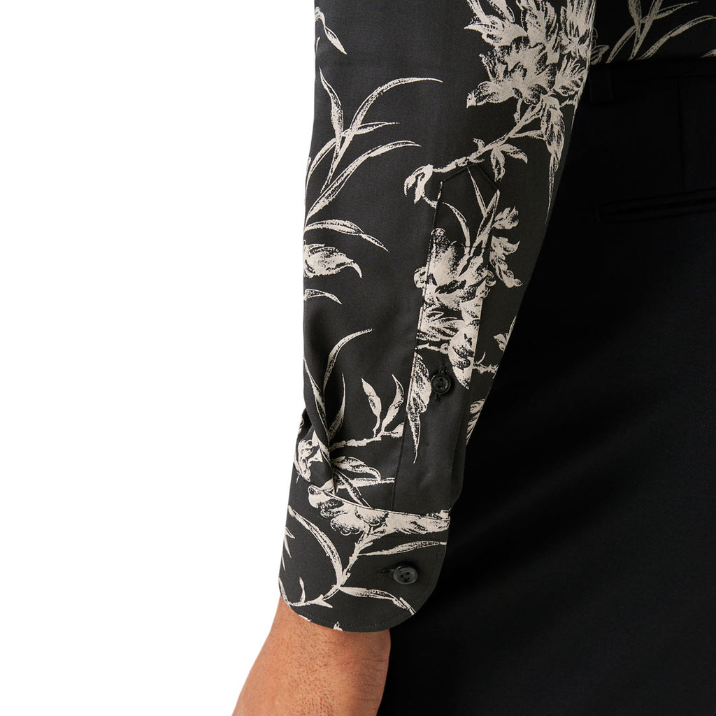Close-up of a long-sleeve button-up shirt sleeve with a black base and white floral print, worn by a model with a black jacket or trousers visible underneath. Eton Shirt available at Sakks Menswear in Southampton.