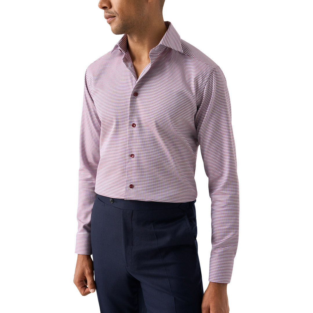 A man wearing a long-sleeve button-down dress shirt with fine horizontal stripes in pink and white, paired with navy trousers, shown against a plain white background. Eton Shirt available at Sakks Menswear in Southampton.