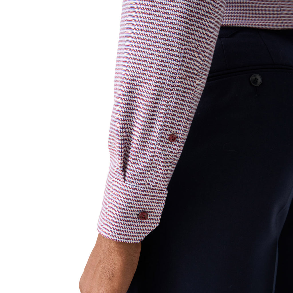 Close-up of a person wearing a long-sleeve dress shirt with a fine pink and white houndstooth pattern, paired with dark navy trousers, against a plain white background. Eton Shirt available at Sakks Menswear in Southampton.