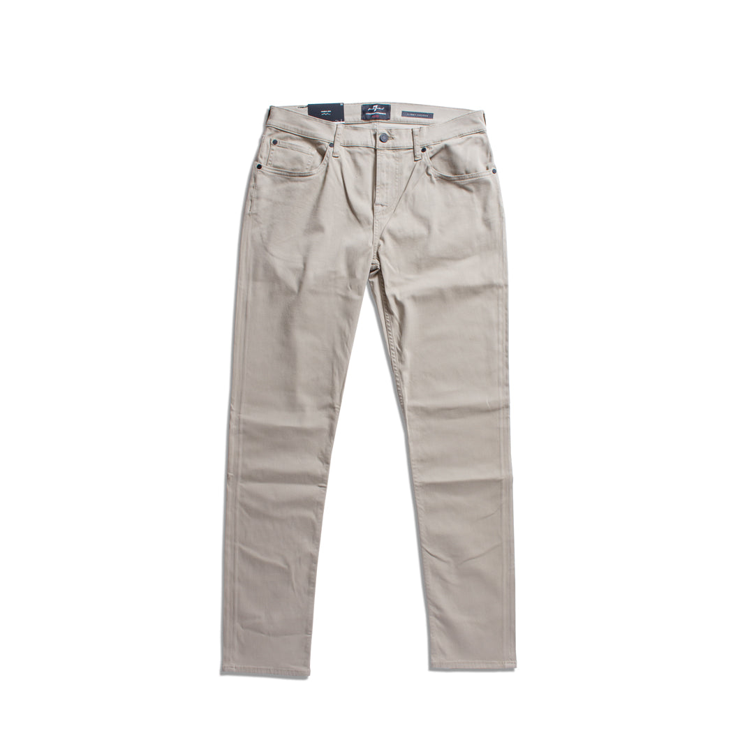 A pair of light beige slim-fit jeans shown flat against a solid white background. 7 For All Mankind Chinos available at Sakks Menswear in Southampton.