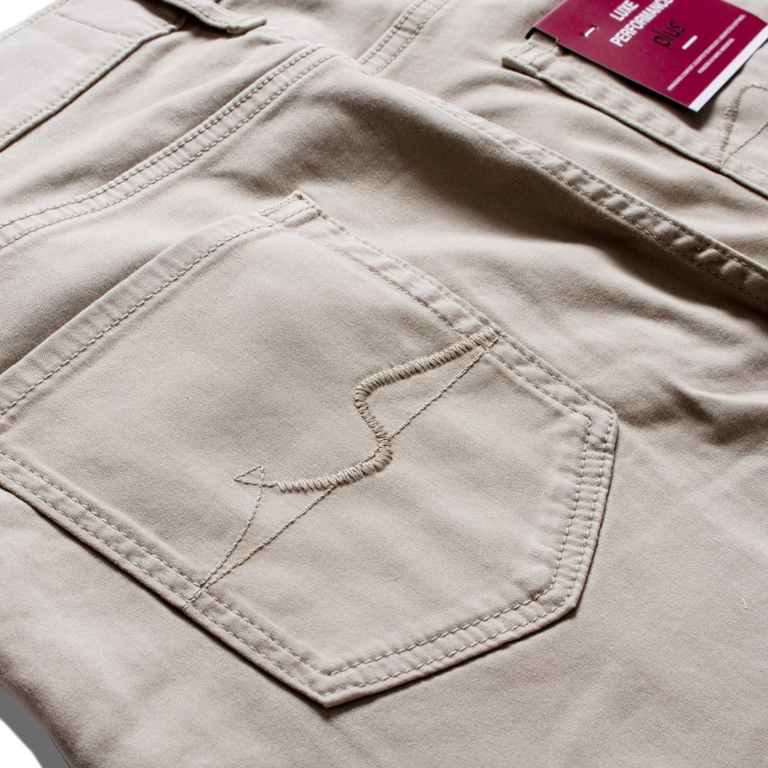 Close-up of a pair of light beige chino pants showing the back pocket with decorative stitching and a magenta brand tag. 7 For All Mankind Chinos available at Sakks Menswear in Southampton.