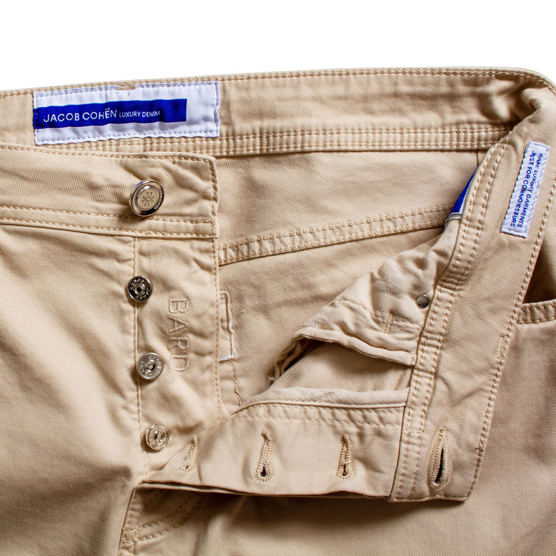 Close-up of khaki denim pants showing the waistband, button fly, pocket, and interior waistband label by Jacobs Cohen. Jacob Cohën Chinos available at Sakks Menswear in Southampton.
