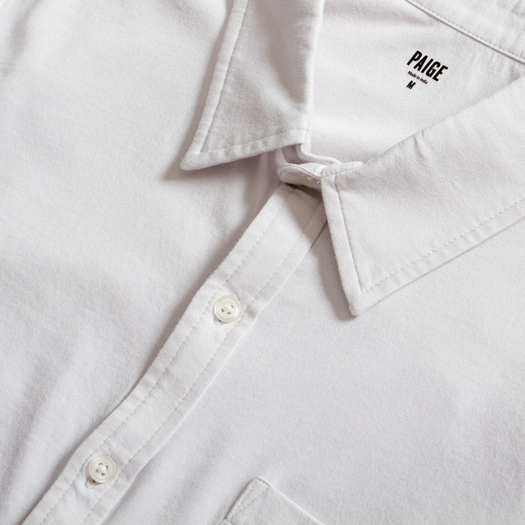 Close-up of a white button-down shirt collar with the brand name PAIGE printed inside the neck, showing white buttons and clean stitching. PAIGE Shirt available at Sakks Menswear in Southampton.