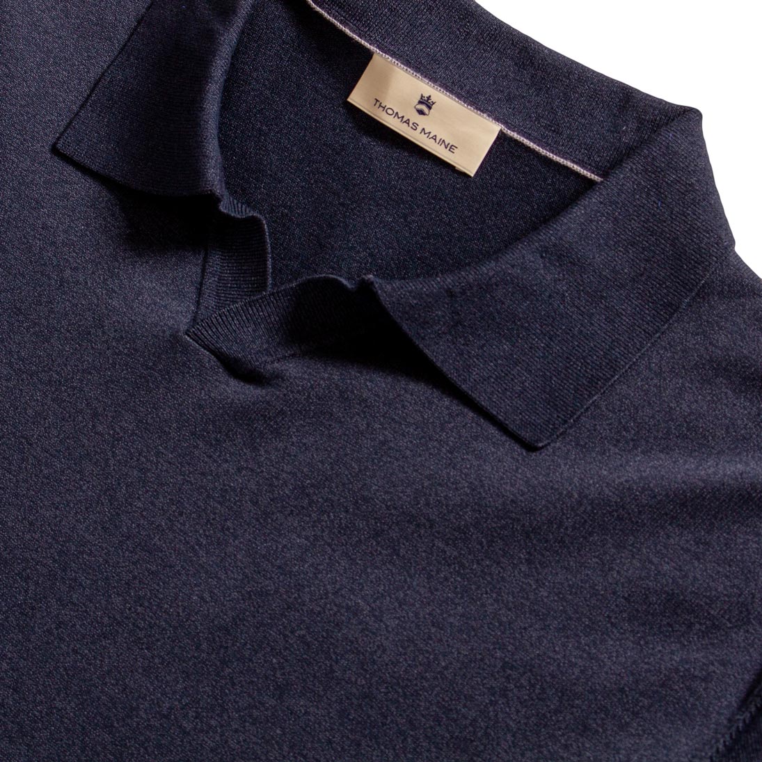 Close-up of a dark navy knit polo shirt collar with a beige Thomas Maine brand label visible inside the neck. Thomas Maine Polo available at Sakks Menswear in Southampton.