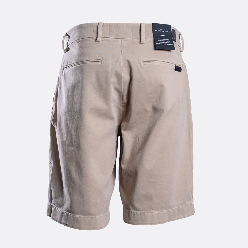 Back view of a pair of men's khaki shorts with a waistband belt loop, rear welt pockets, and a small black brand tag on the right side, shown on a light gray background. - 7 For All Mankind Comfort Sateen Chino Short in Mud. Sakks Menswear