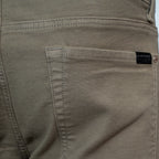 Close-up of the back pocket of a pair of khaki-colored denim jeans, showing the stitching and a small black brand label. 7 For All Mankind. Sakks Menswear Southampton.