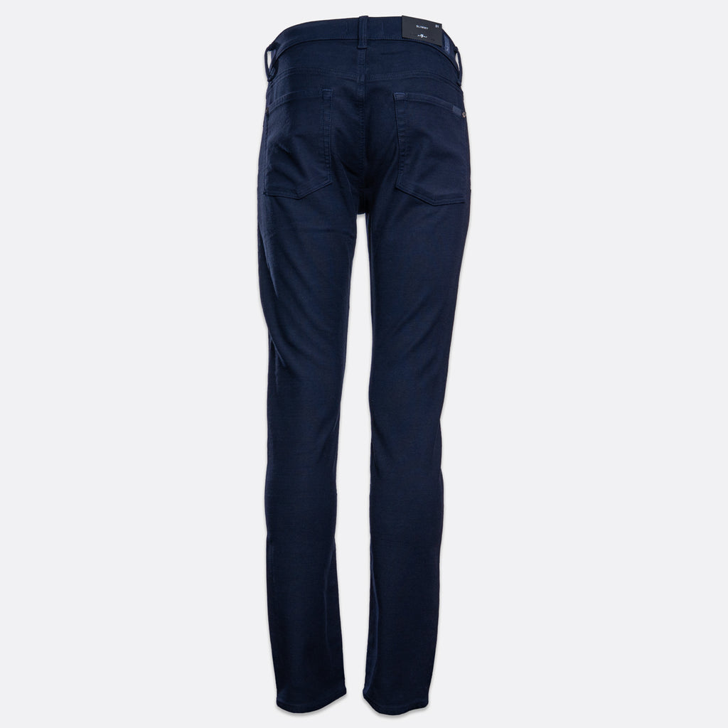 A pair of dark navy blue jeans shown from the waist down on a light grey background. 7 For All Mankind Slimmy Jeans. Sakks Menswear Southampton.