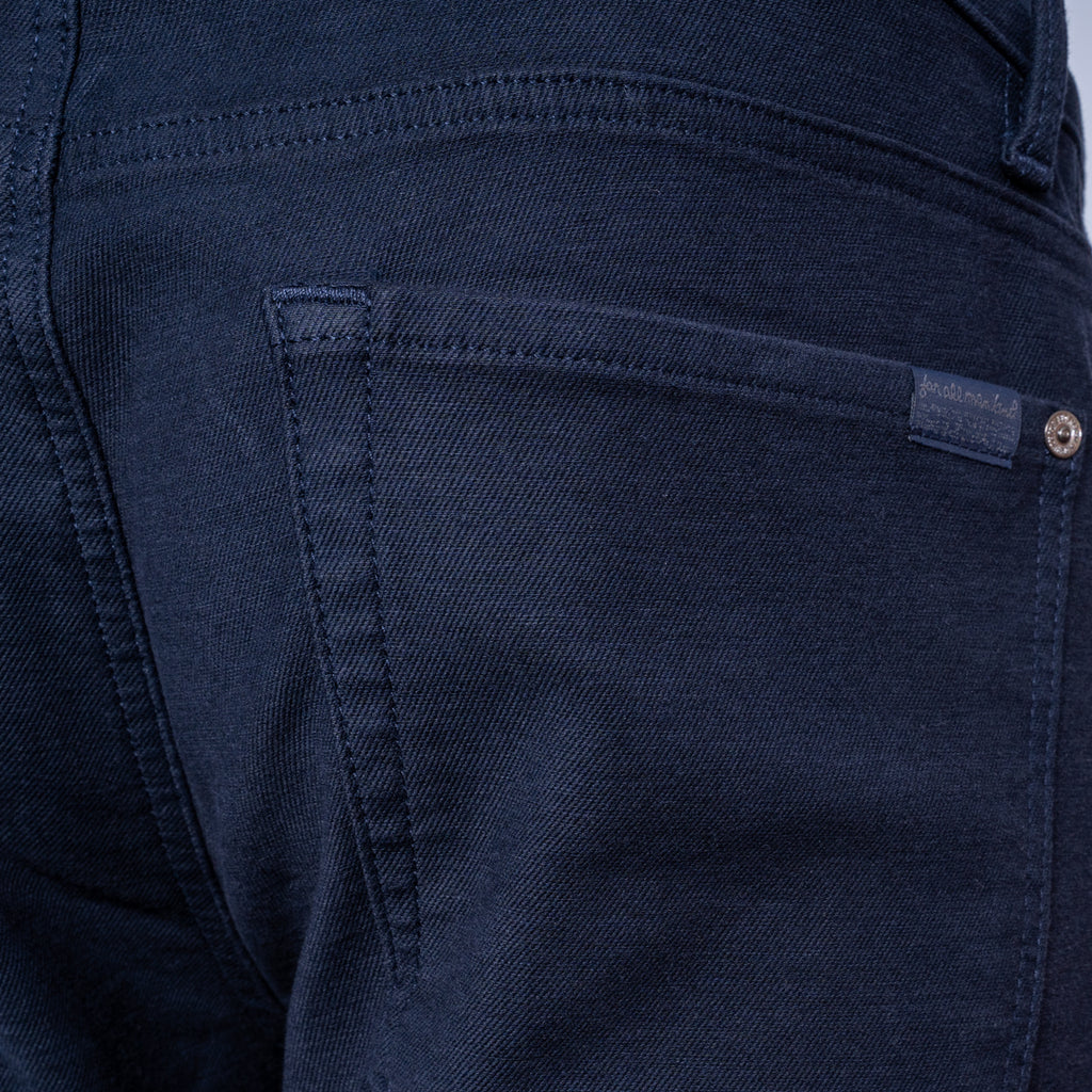 Close-up of the back pocket of dark navy blue denim jeans, showing the stitching and a small metal button closure. 7 For All Mankind Slimmy Jeans. Sakks Menswear Southampton.