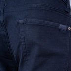 Close-up of the back pocket of dark navy blue denim jeans, showing the stitching and a small metal button closure. 7 For All Mankind Slimmy Jeans. Sakks Menswear Southampton.