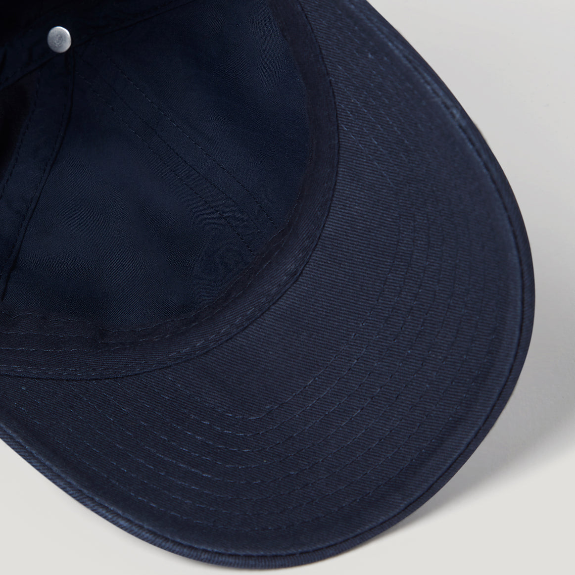 Close-up of a dark navy blue baseball cap showing the curved brim, stitched panel seams, and a small silver metal eyelet. Belstaff Cap. Sakks Menswear Southampton.