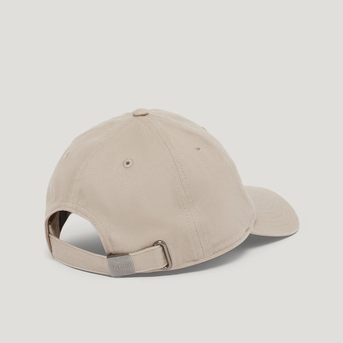 A light beige baseball cap shown from a rear three-quarter angle, featuring an adjustable fabric strap with a silver metal buckle, set against a solid light gray background. Belstaff Cap. Sakks Menswear Southampton.