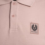 Close-up of a light pink textured polo shirt with a black Belstaff winged logo patch on the left chest. Belstaff Polo. Sakks Menswear Southampton.