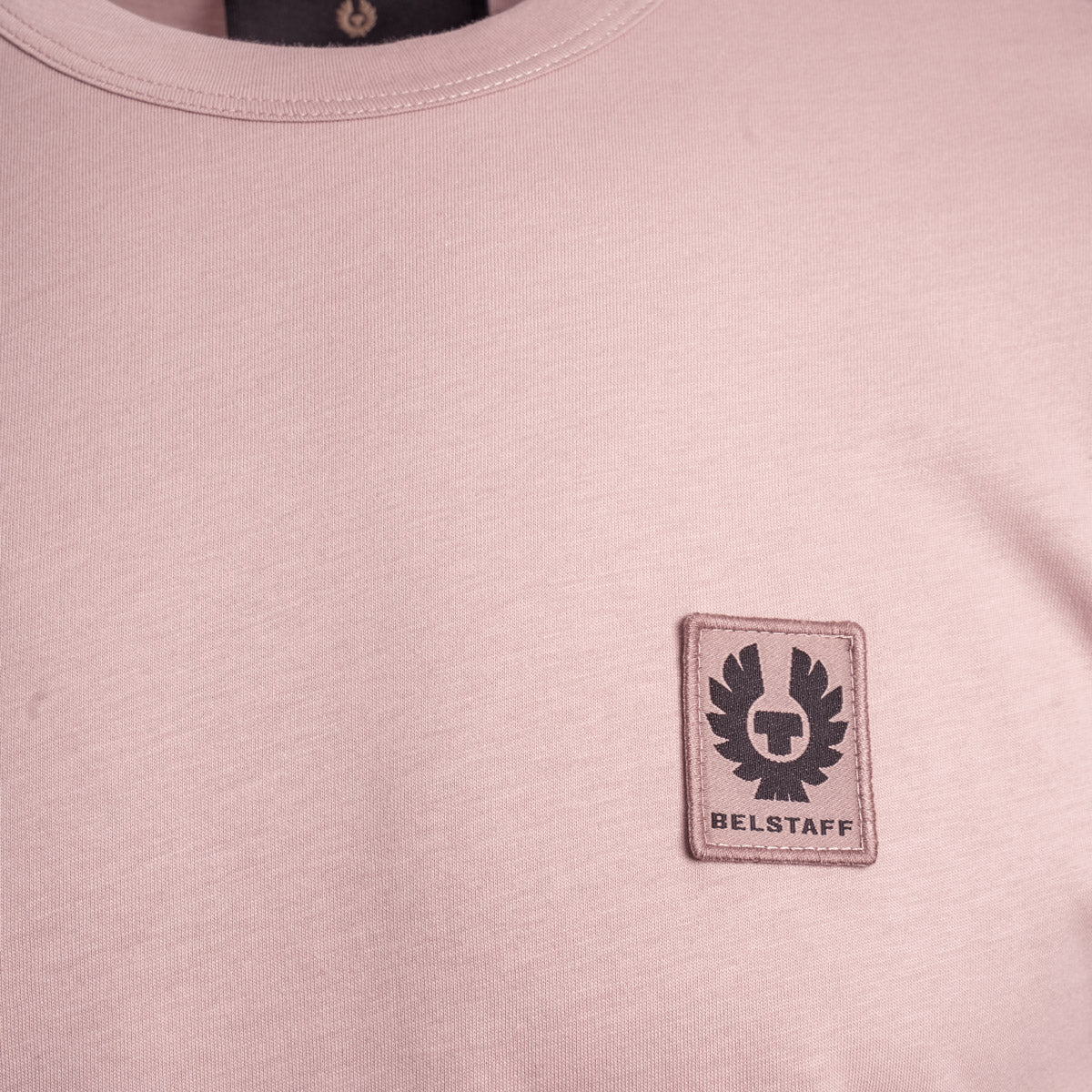Close-up of a dusty pink crewneck t-shirt featuring a rectangular embroidered BELSTAFF logo patch on the left chest. Belstaff T-Shirt. Sakks Menswear Southampton.