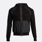A black zip-up hooded jacket with contrasting dark gray front pockets and shoulder panels, shown on a light gray background. Belstaff Hoodie. Sakks Menswear Southampton.