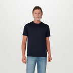 A man wearing a dark navy blue crew-neck t-shirt with a small tonal embroidered logo on the left chest, paired with light-wash blue jeans, standing against a plain white studio background. Belstaff T-Shirt. Sakks Menswear Southampton.