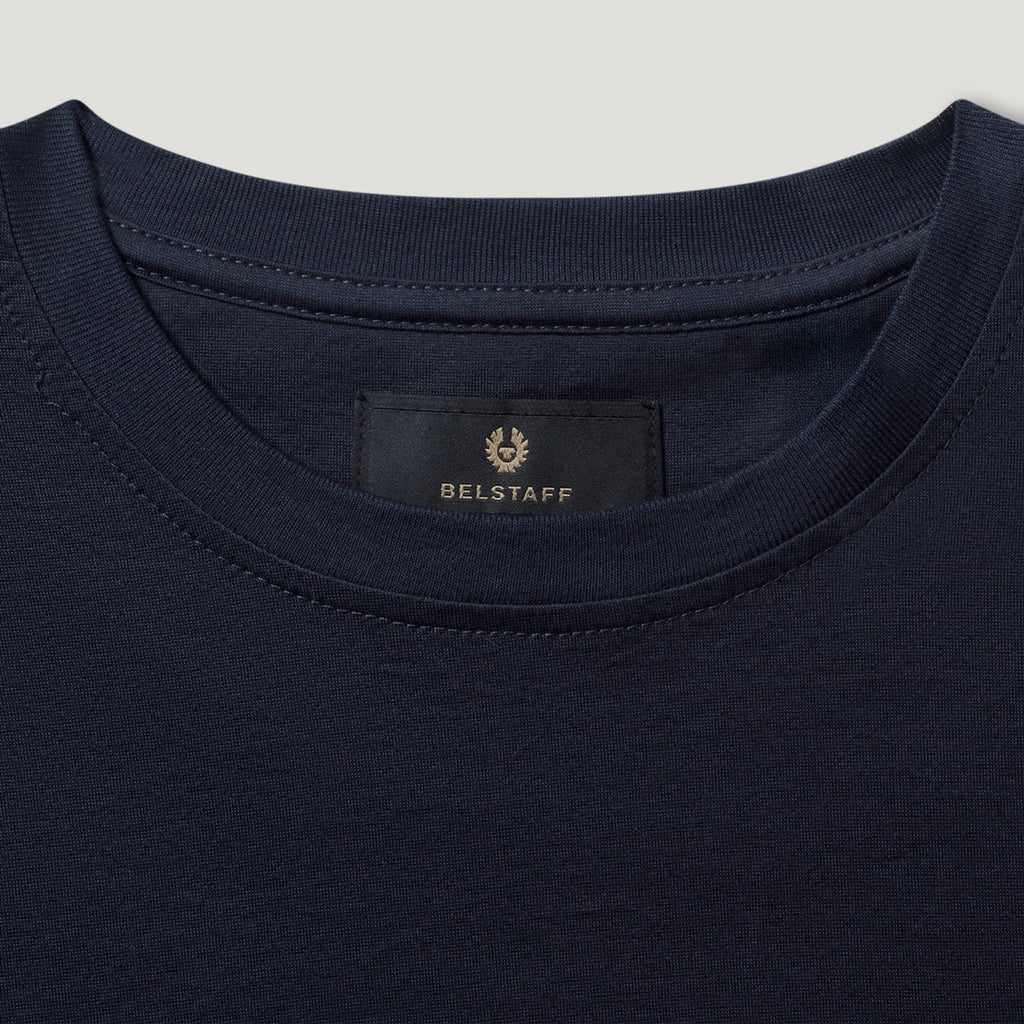 Close-up of a navy blue crewneck t-shirt showing the inner neck label with the BELSTAFF brand name and logo. Belstaff T-Shirt. Sakks Menswear Southampton.