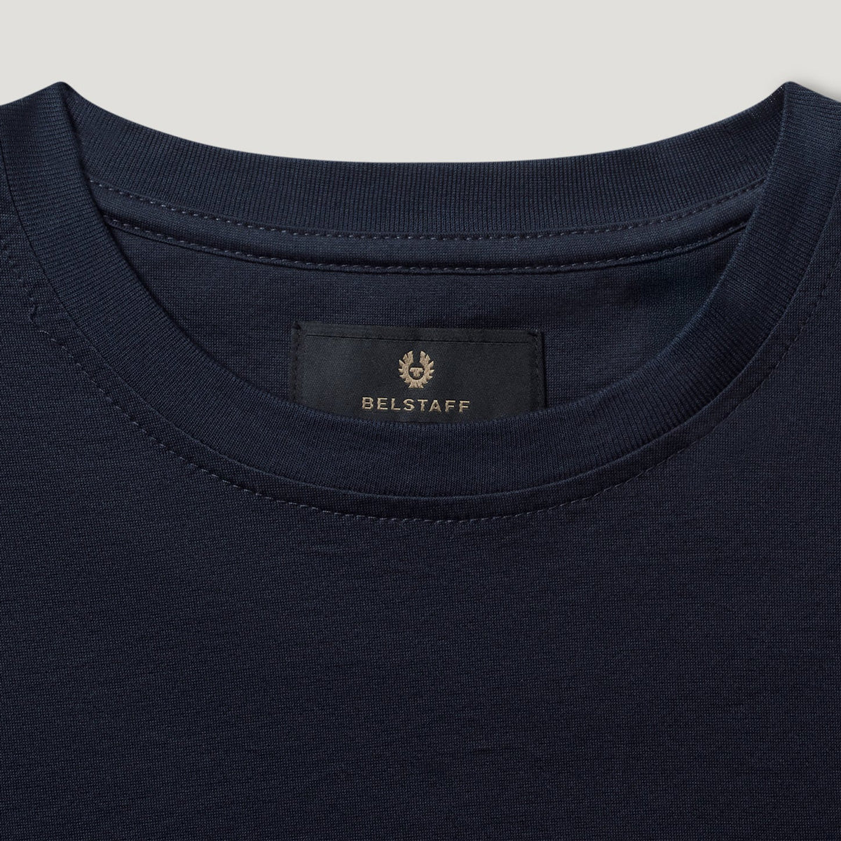 Close-up of a navy blue crewneck t-shirt showing the inner neck label with the BELSTAFF brand name and logo. Belstaff T-Shirt. Sakks Menswear Southampton.