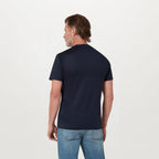 A man viewed from the back wearing a dark navy blue short-sleeve crewneck t-shirt and light blue jeans, standing against a plain white studio background. Belstaff T-Shirt. Sakks Menswear Southampton.