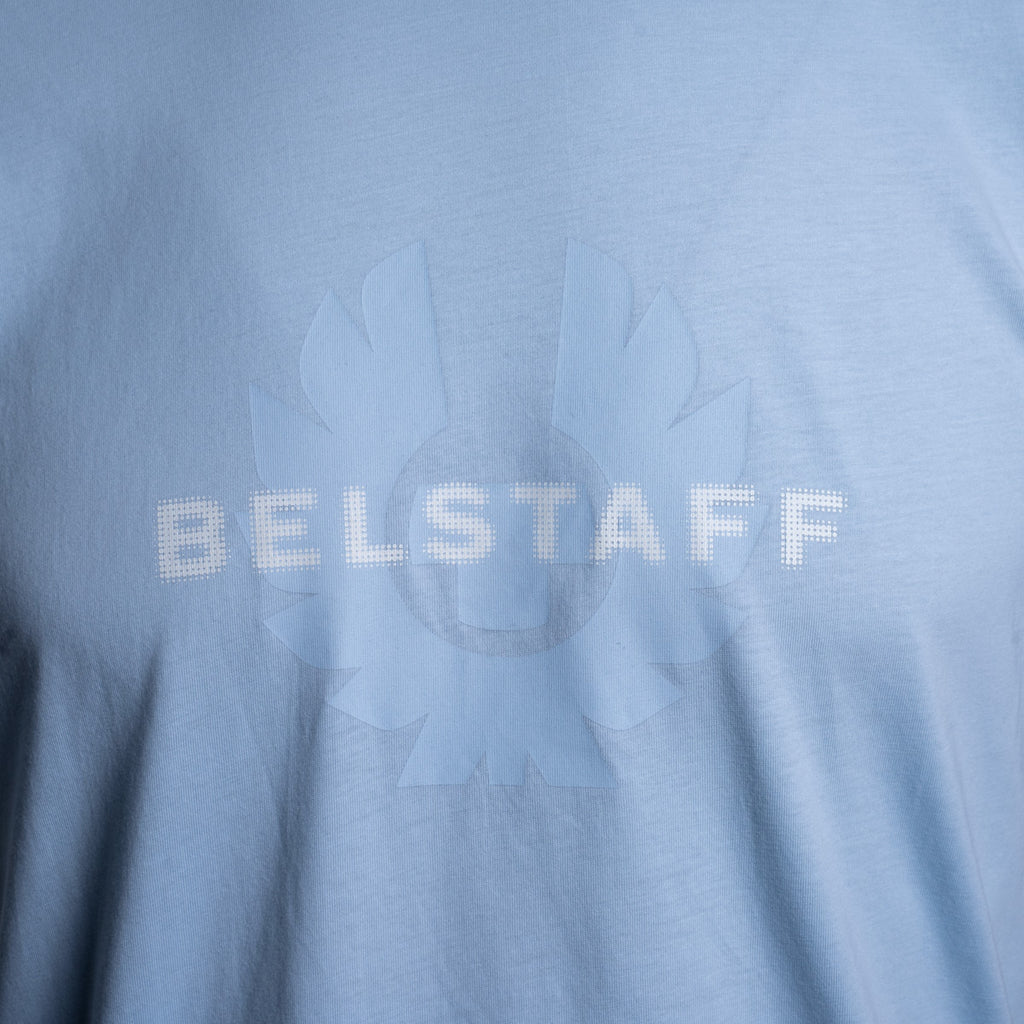 Close-up of a light blue t-shirt featuring a tonal, semi-transparent graphic of a sunburst with the word 'BELSTAFF' printed across the center. Belstaff T-Shirt. Sakks Menswear Southampton.