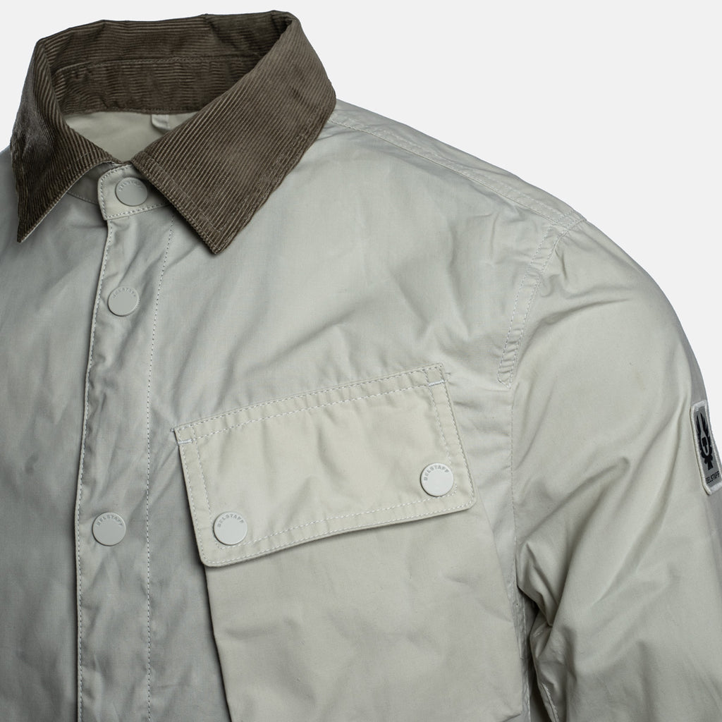 Close-up of a light gray button-up shirt jacket with a contrasting brown corduroy collar and a flap chest pocket with snap buttons. Belstaff Jacket. Sakks Menswear Southampton.