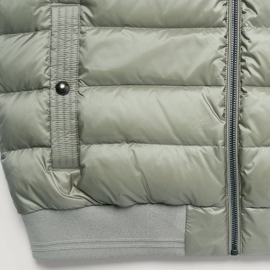 Close-up of a light sage green puffer jacket showing horizontal quilting, a vertical zippered pocket with a snap tab, a black zipper, and ribbed knit cuffs. Belstaff Gilet. Sakks Menswear Southampton.