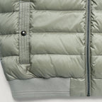 Close-up of a light sage green puffer jacket showing horizontal quilting, a vertical zippered pocket with a snap tab, a black zipper, and ribbed knit cuffs. Belstaff Gilet. Sakks Menswear Southampton.