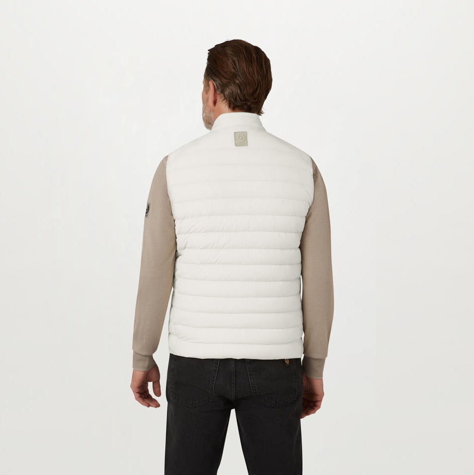 A man viewed from the back wearing a white quilted puffer vest over a beige long-sleeve shirt and black pants, against a plain white studio background. Belstaff Gilet. Sakks Menswear Southampton.