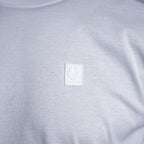 Close-up of a light gray heather crewneck t-shirt featuring a square white embroidered patch on the chest with a winged emblem and the text 'BELSTAFF'. Belstaff T-Shirt. Sakks Menswear Southampton.