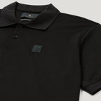 Close-up of a black short-sleeve polo shirt with a collar, two-button placket, and a small square chest patch logo on a light gray background. Belstaff Steel Polo. Sakks Menswear Southampton.