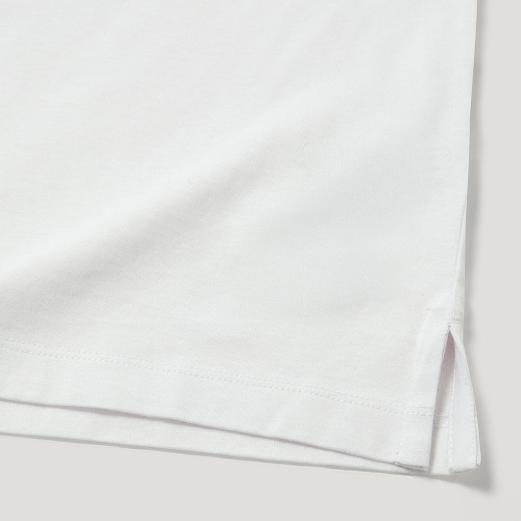 Close-up of a white folded garment, showing the hem with a small side slit and fine stitching against a light neutral background. Belstaff Polo. Sakks Menswear Southampton.