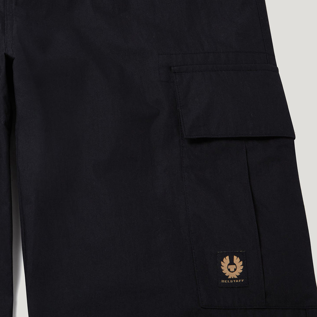 Close-up of dark navy cargo pants showing a side pocket with a small tan Deloitor logo patch on the lower corner. Belstaff Cargo Pants. Sakks Menswear Southampton.