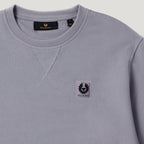 A close-up of a light gray crewneck sweatshirt by Bellruff, featuring a small black and white embroidered logo patch on the left chest and a black neck label. Belstaff Sweatshirt. Sakks Menswear Southampton.